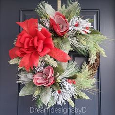 a wreath with red flowers and greenery hanging on the front door for holiday decor