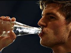 a man drinking water out of a clear glass in front of a black background,