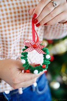 a woman holding a christmas wreath ornament in her hands with a red ribbon