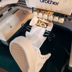 a pair of white shoes sitting on top of a machine with the word brother printed on it