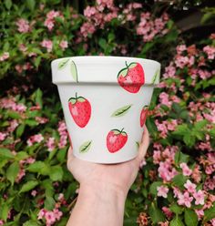 a hand holding up a cup with strawberries on it in front of pink flowers