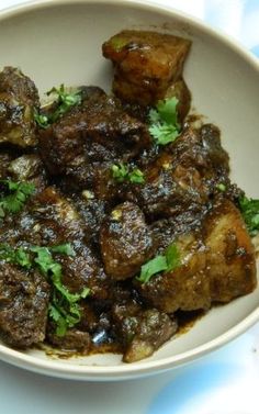 a white bowl filled with meat and garnished with cilantro on top