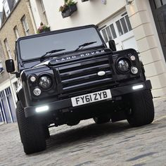 a black land rover is parked in front of a building on a cobblestone street