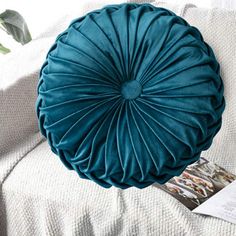 a blue round pillow sitting on top of a white couch next to a magazine and plant