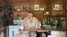 a woman sitting at a table in a kitchen drinking from a cup with her legs crossed