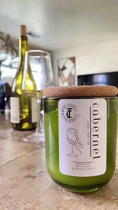 a green candle sitting on top of a counter next to wine bottles and glassware