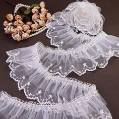 two pieces of white lace with flowers and pearls on the table next to each other