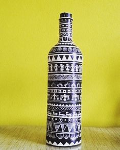 a black and white vase sitting on top of a wooden table next to a yellow wall