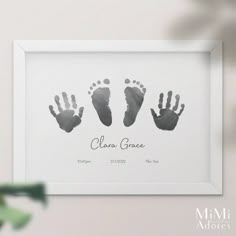 a white frame with three handprints on it and the words clara grace written in black ink