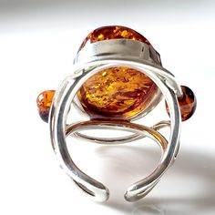 The Handcrafted Large Amber ring is just stunning. The Large Oval Amber Ring is a stunning piece of jewelry featuring an oval-shaped amber gemstone as its centerpiece. The amber gemstone, known for its warm and rich color, adds a touch of elegance and natural beauty to the ring. Surrounding the amber gemstone, on each side, are two round beads that complement the main stone and add a balanced and symmetrical look to the design. The combination of the oval amber gemstone and the round beads creat Modern Amber Oval Ring, Oval Amber Jewelry, Oval Amber Cabochon Ring, Amber Oval Cabochon Rings, Modern Oval Amber Jewelry, Modern Amber Oval Jewelry, Amber Rings With Natural Stones, Amber Citrine Oval Ring, Oval Citrine Amber Rings