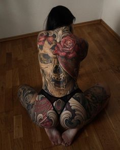 a woman sitting on the floor with tattoos on her body and hands behind her head