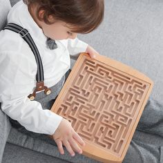 a little boy sitting on a couch holding a piece of wood with mazes in it