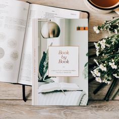 an open book sitting on top of a wooden table next to a cup of coffee