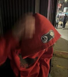 a person wearing a red jacket and hat on the street with their head tilted to the side