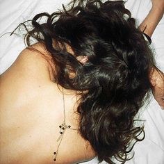 a woman laying in bed with her back turned to the camera and wearing a white shirt