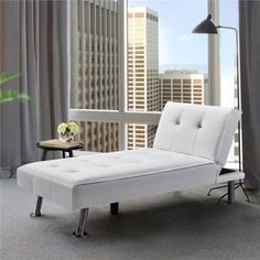 a white chaise lounger sitting in front of a window overlooking a cityscape