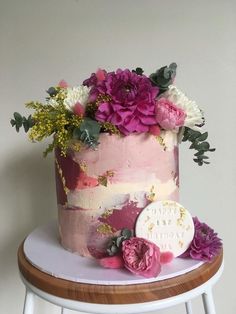 a pink and white cake with flowers on top sitting on a small stool next to a wall