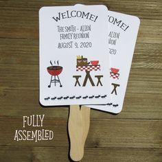 two personalized hand fans with bbq grills on them are sitting on a wooden table