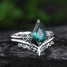 a ring with an emerald colored stone in the center on top of a piece of wood