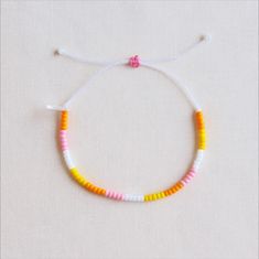 a white string bracelet with yellow and pink beads on it's end, sitting on a plain surface