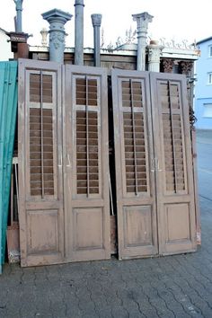 three wooden doors with shutters on the side of a street next to a building