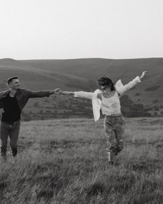 two people running through a field with their arms spread out in the air and holding hands