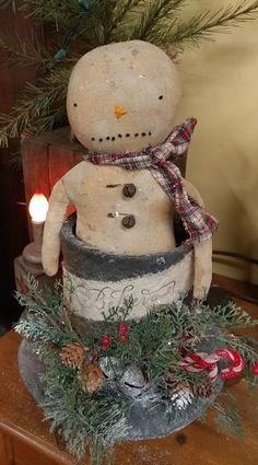 a snowman sitting on top of a wooden table next to a candle and potted plant