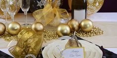 a table topped with plates and glasses filled with gold colored confetti next to wine bottles