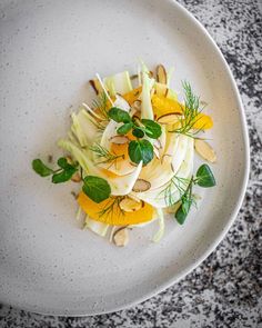 a white plate topped with food on top of a marble countertop next to a knife and fork