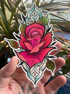 a hand holding a sticker with a pink rose on it's center and green leaves in the background