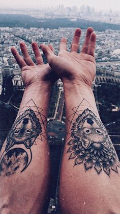 two people with tattoos on their arms are looking out over the city from atop a tall building