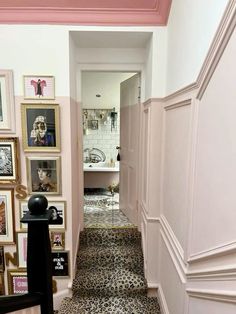 the hallway is decorated in pink and white with pictures on the wall above it, along with an ornate stair case