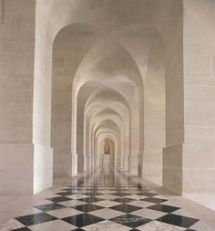 a long hallway with black and white checkered flooring on the walls, leading to an archway