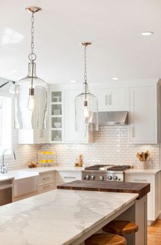 a kitchen with marble counter tops and two pendant lights hanging from it's ceiling