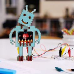 a robot made out of paper sitting on top of a table next to some wires