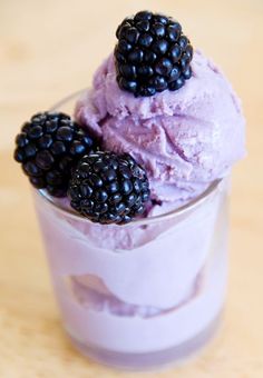 two scoops of ice cream with blackberries on top, in a glass cup