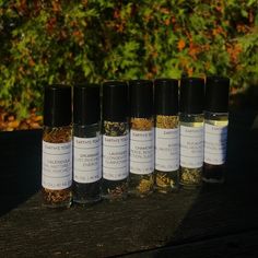 five bottles filled with different types of herbs on top of a wooden table next to bushes