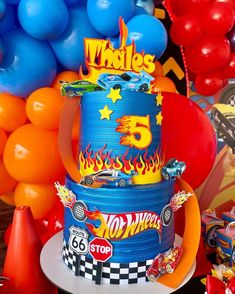 a birthday cake with hot wheels on top and balloons in the background at a race themed birthday party