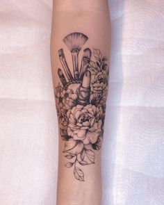 a woman's leg with flowers and makeup brushes on her left arm, which is covered in black ink