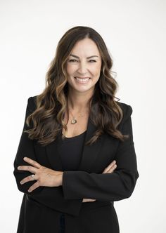 a woman with her arms crossed smiling at the camera while wearing a black blazer