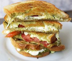 there is a sandwich that has been cut in half on a white plate with tomatoes and pesto