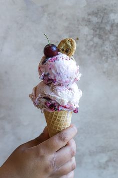 a person holding up an ice cream cone with cherries on top