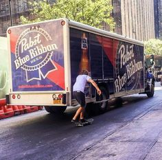 a man riding a skateboard next to a truck on a city street in front of tall buildings