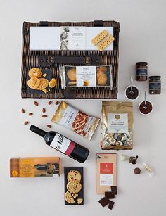 a wicker basket filled with different types of food and condiments next to bottles of wine