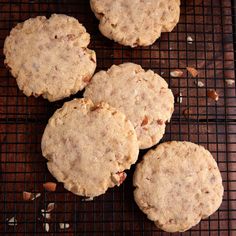 four cookies cooling on a wire rack with nuts scattered around them and one cookie has been cut in half