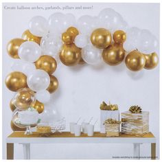 gold and white balloons are hanging from the wall above a table with presents on it