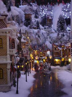 a street with lots of buildings and lights covered in snow next to christmas tree decorations