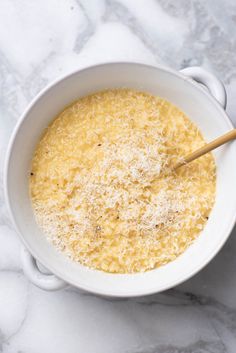 a white bowl filled with cheese on top of a marble counter next to a wooden spoon