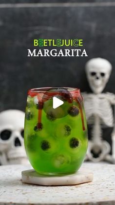 a green drink with fruit in it sitting on a table next to two skeleton heads