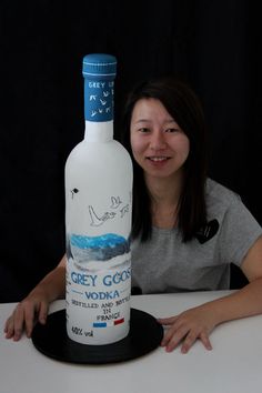 a woman sitting at a table with a bottle of grey goose vodka on top of it